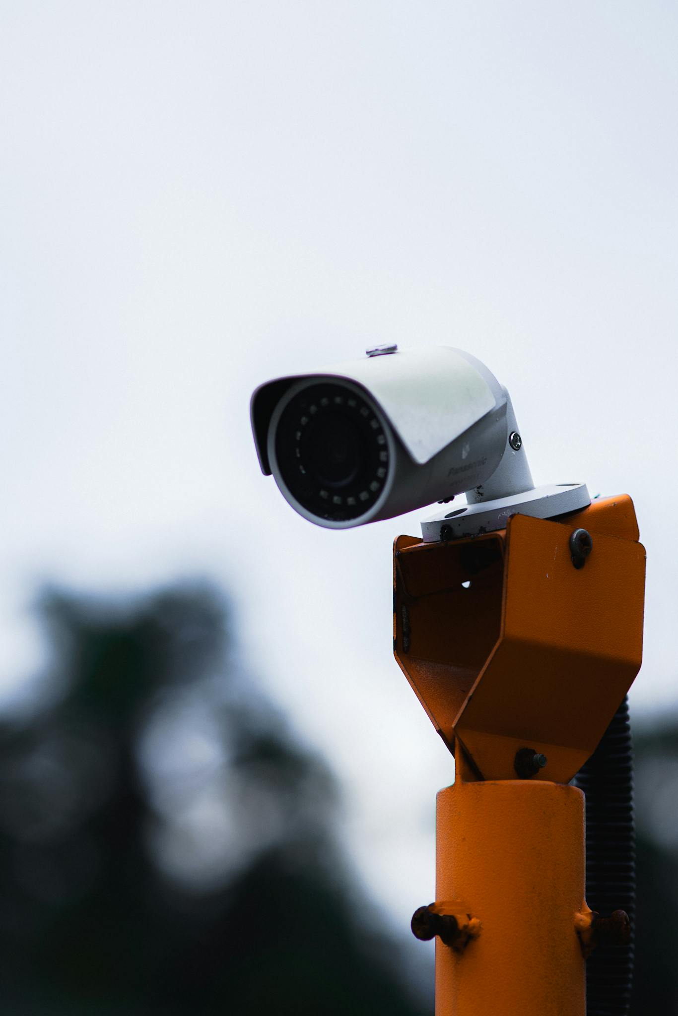 A security camera mounted on an orange stand against a blue sky.